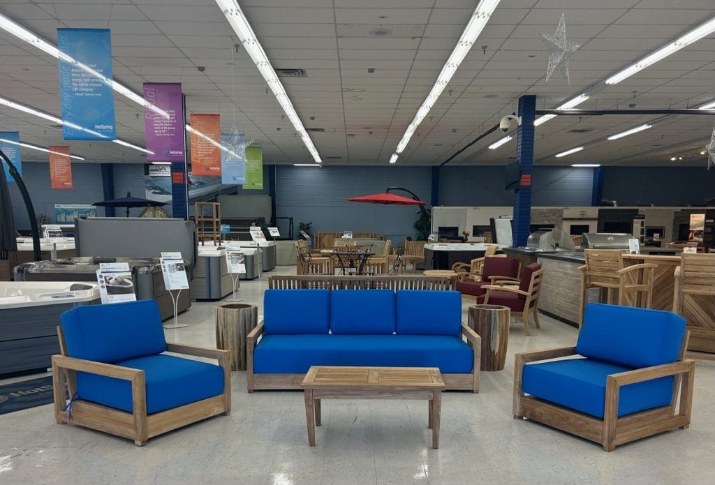 Interior of a showroom - showing 2 patio chairs, a patio couch, patio table in the foreground, and an assortment of patio furniture and hot tubs in the background