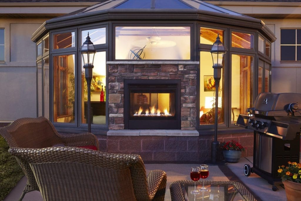 Outdoor living example - fireplace built into the outside wall of a house next to patio furniture and a BBQ