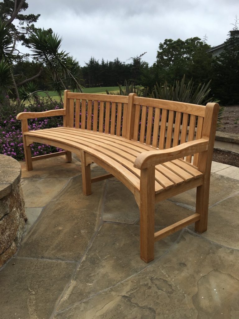 Teak bench in a backyard in front of flowers