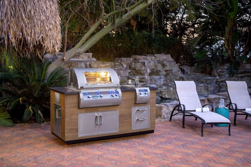 Outdoor kitchen island with double door setup next to 2 patio loungers in front of rock waterfall display